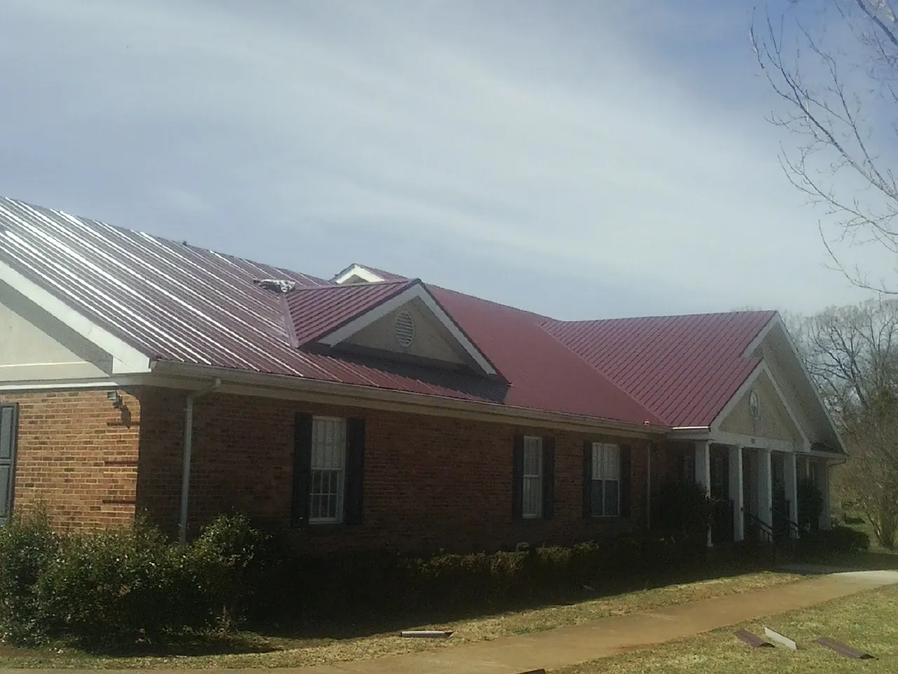 Red metal roof with gabled entries on a long brick building, from a Hail Damage Roof Repair job in Punxsutawney