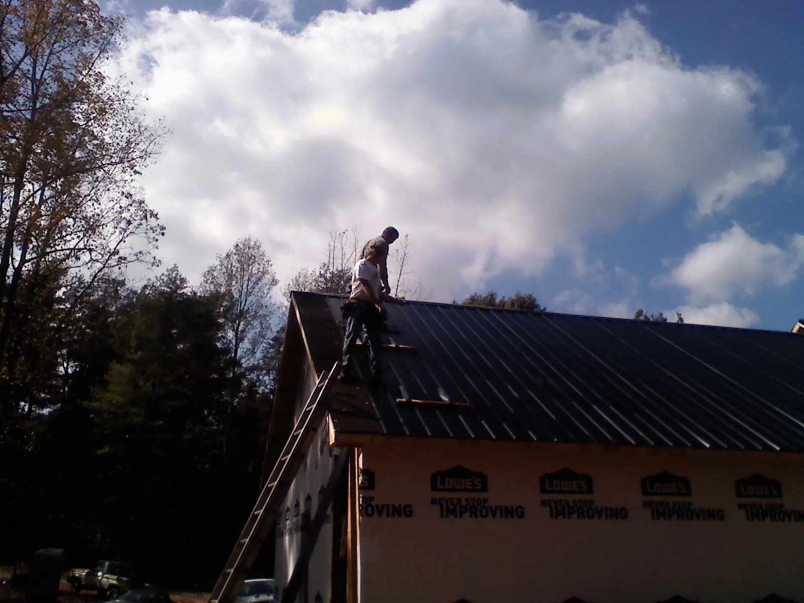 Roofer fastening dark metal panels high against a cloudy sky, from a Roof Inspection job in Punxsutawney