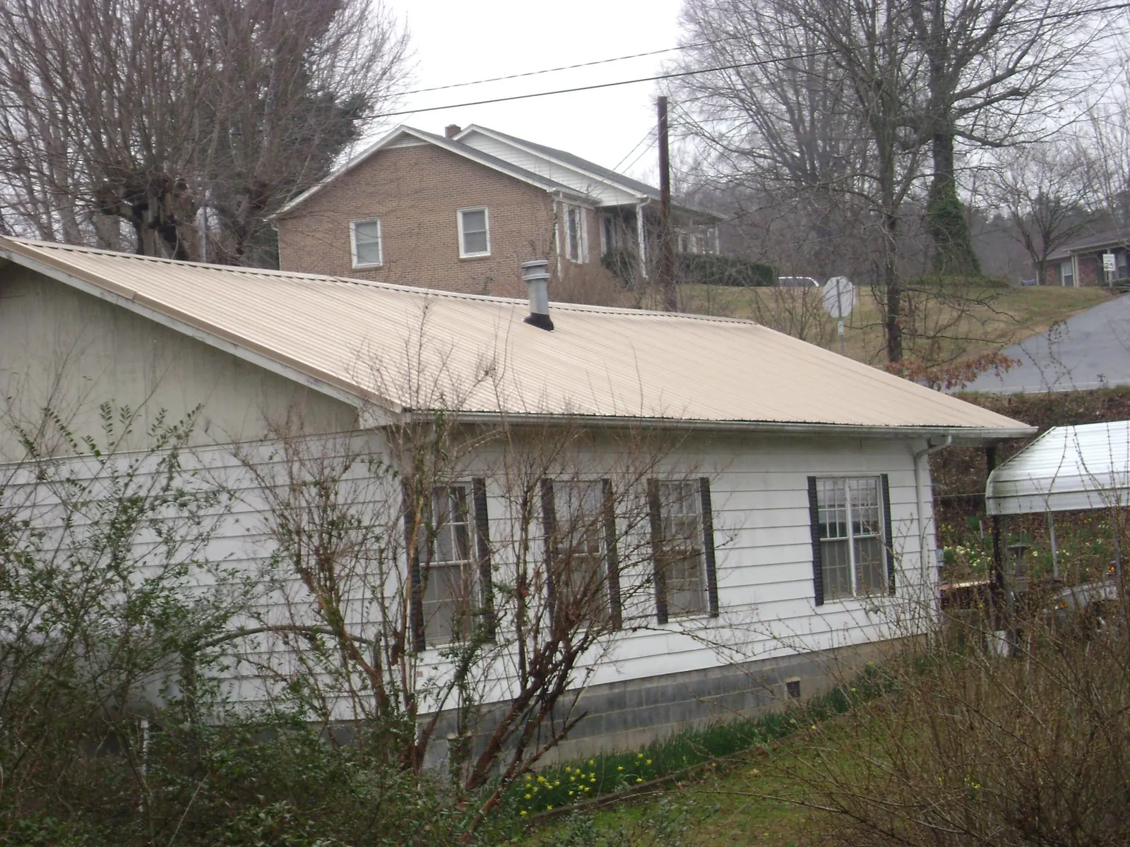 Tan metal roof on a white sided house set into a hillside — Commercial Roofing by Roofing Brothers in Punxsutawney